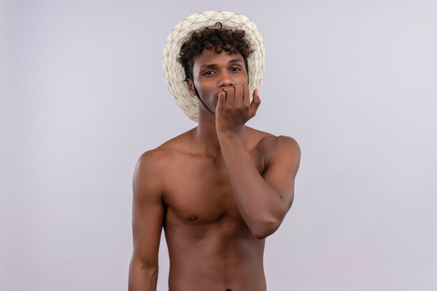 A sad young handsome dark-skinned man with curly hair wearing sun hat keeping hand on face while  