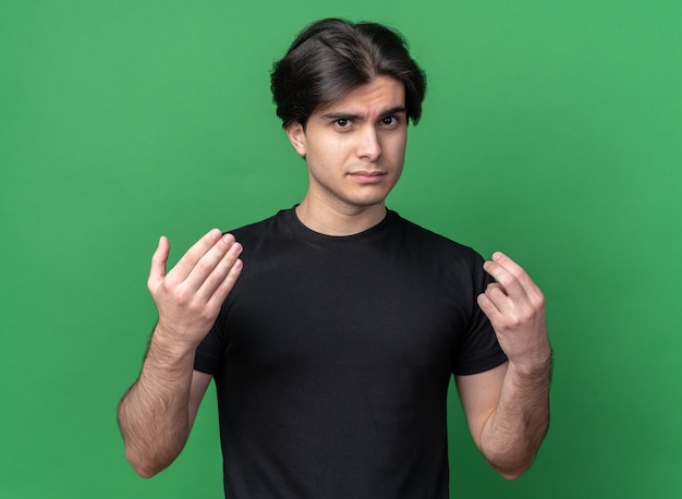 Free photo sad young handsome guy wearing black t-shirt showing tip gesture isolated on green wall