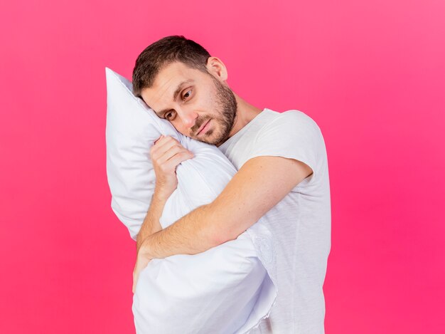Sad young ill man hugged pillow isolated on pink background