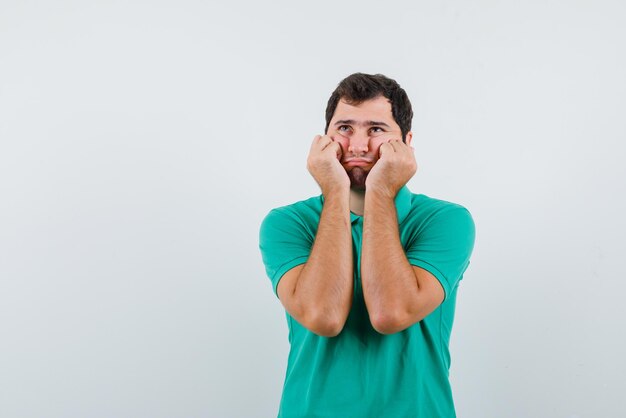 The sad young man is thinking by putting fists on cheeks on white background