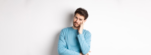 Free photo sad young man looking frustrated touching temple of head and frowning uneasy standing against white