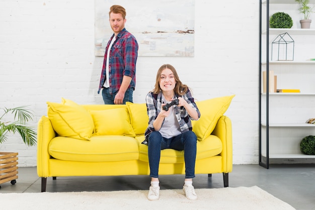 Sad young man looking at smiling woman enjoying playing the video game at home