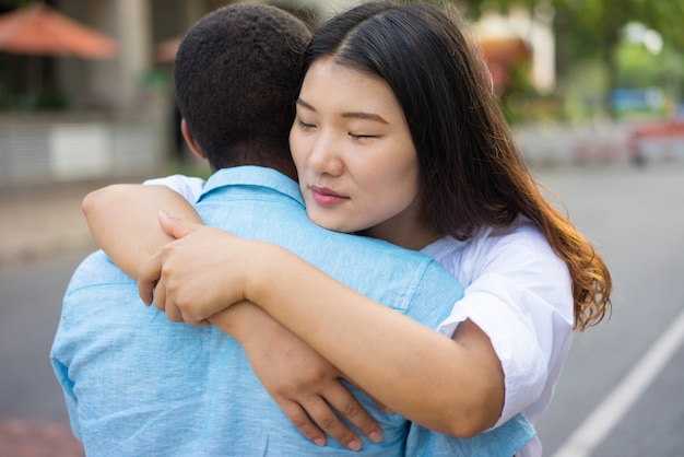 Sad young multiethnic couple or friends hugging outdoors.