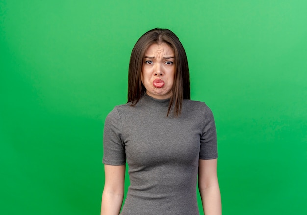 Sad young pretty woman standing and looking at camera isolated on green background with copy space