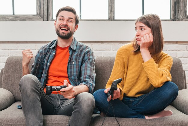 Sad young woman looking at her husband playing the video game with joystick