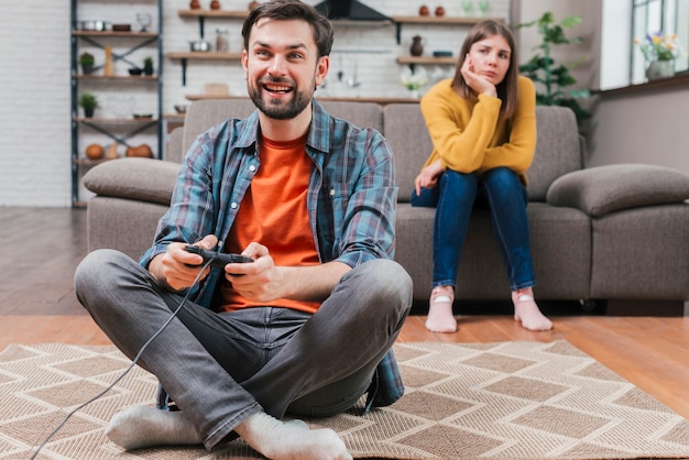 Sad young woman looking at man playing the video game with joystick