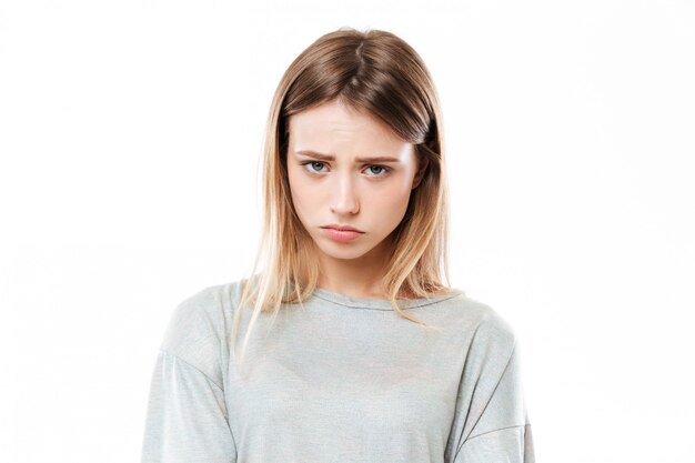 Sad young woman standing isolated over white wall