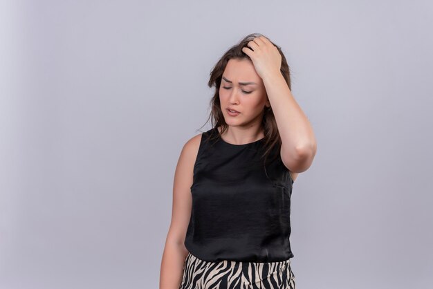 Sad young woman wearing black undershirt grabbed head on white wall