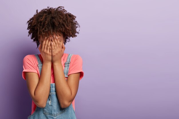 sad young woman with an afro posing in overalls