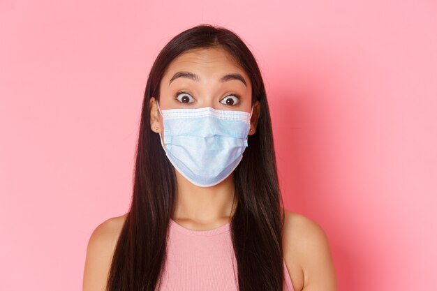安全な観光、コロナウイルスのパンデミック中の旅行、ウイルスの概念の防止。医療マスクで驚いて驚いたアジアの女の子の観光客のクローズアップは眉を上げ、驚いているように見えます。