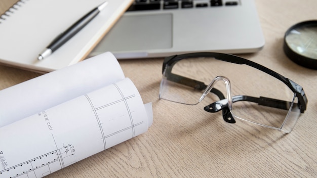 Safety glasses and blueprint near laptop and notebook