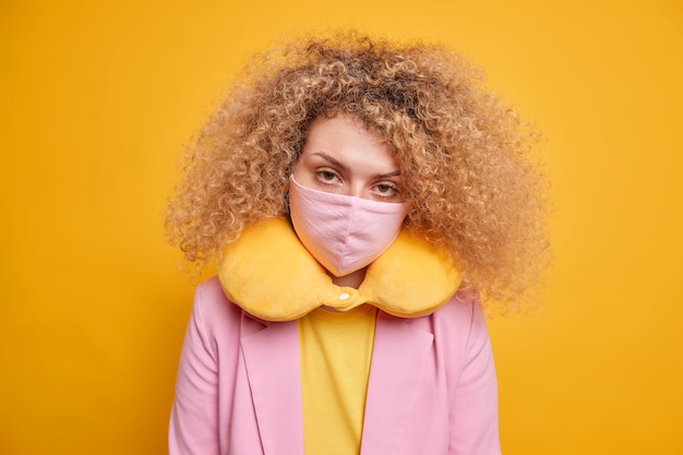ウイルス発生時の安全対策。真面目な女性は自信を持って保護マスクを着用し、鮮やかな黄色の壁に服の首の枕のポーズを合わせます。封鎖とcovid19