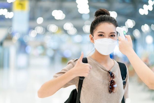 Safety travel new normal lifestyleasian female traveller wear casual cloth temperature check detect covid19 at airport terminal before going abroad travel with blur airport departure terminal