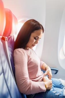 Безопасное путешествие. молодая азиатская женщина прикрепляет пояса пока сидящ в сидении самолета.