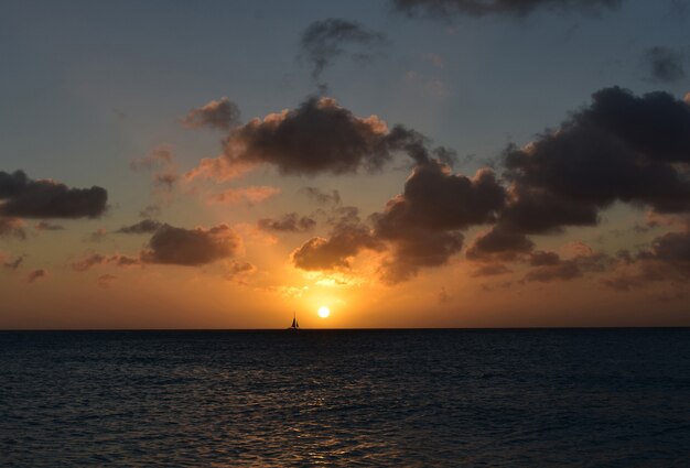 Sailboat sailing in front of the setting sun in Aruba.