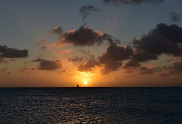 Sailboat sailing in front of the setting sun in Aruba.
