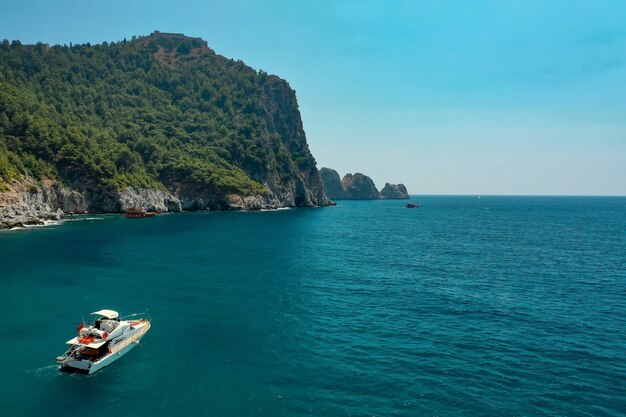 美しい大きな山の上の夕方の日光の下で海のヨット、贅沢な夏の冒険、地中海、トルコでのアクティブな休暇