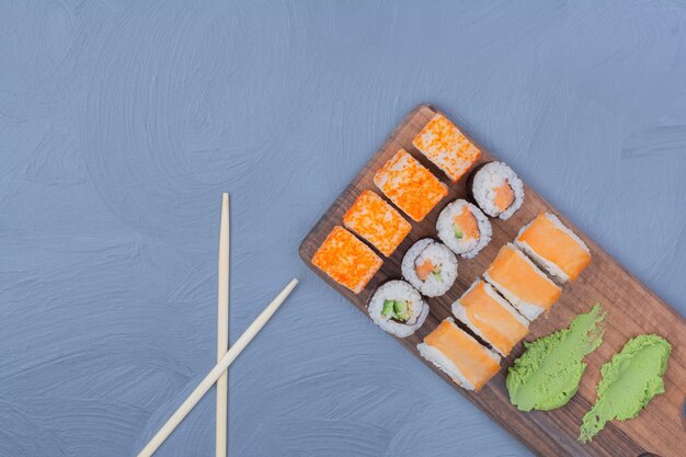 Sake maki and philadelphia rolls with wasabi sauce on a wooden platter