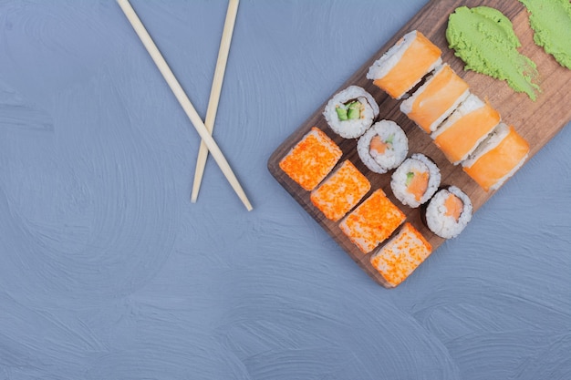 Sake maki and philadelphia rolls with wasabi sauce on a wooden platter