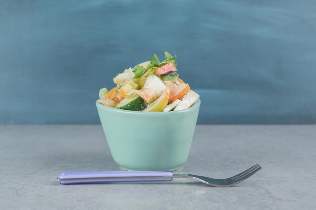 Salad in a blue cup with mixed chopped vegetable and fruits.
