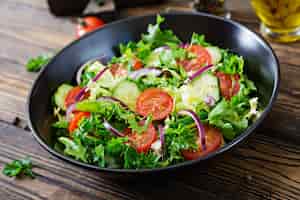 Foto gratuita insalata di pomodori, cetrioli, cipolle rosse e foglie di lattuga. menù vitaminico estivo salutare. alimenti vegetali vegani. tavolo da pranzo vegetariano.