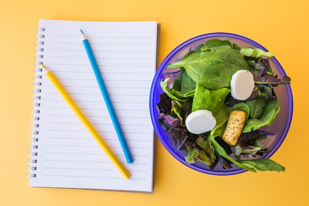 Salad near pencils and notebook