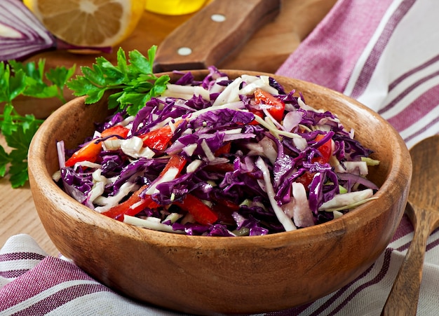 Salad of red and white cabbage and sweet red pepper, seasoned with lemon juice and olive oil in wooden bowl