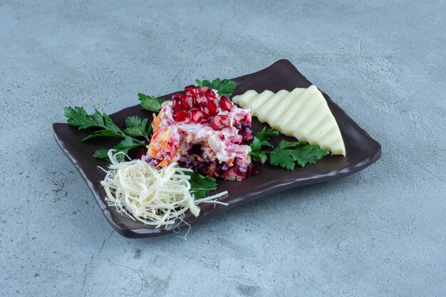 Salad served with sliced and grated cheese on a black platter on marble.