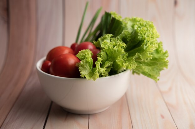 Salad of tomatoes and spring onions in a white cup on a wooden floor.