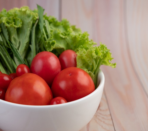 Salad of tomatoes and spring onions in a white cup on a wooden floor.