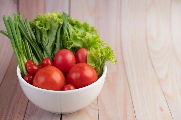 Salad of tomatoes and spring onions in a white cup on a wooden floor.