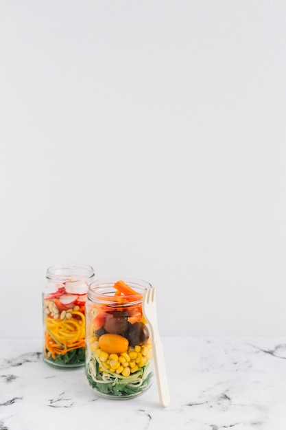 Salad vegetables in two mason jar with fork against white background