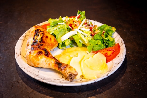 Salad with chicken thigh and salad on a black background, on a white plate