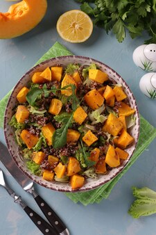 Salad with quinoa, pumpkin and arugula in a plate on light blue background. view from above