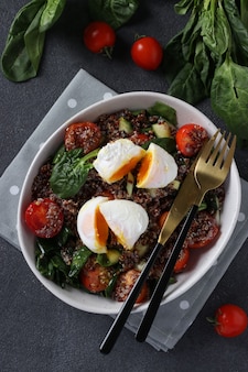 Salad with quinoa, spinach, poached eggs and cherry tomatoes in a plate on gray background. healthy eating. vertical format