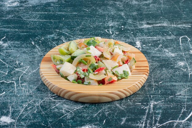 Salad on a wooden platter with chopped ingredients and herbs. 