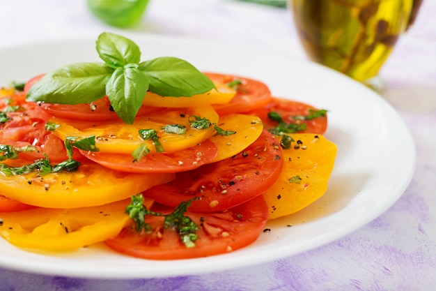 Salad of yellow and red tomato with Basil pesto on a light table.