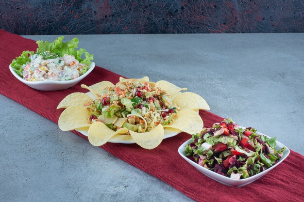 Salads garnished with lettuce leaf and potato chips on marble table.