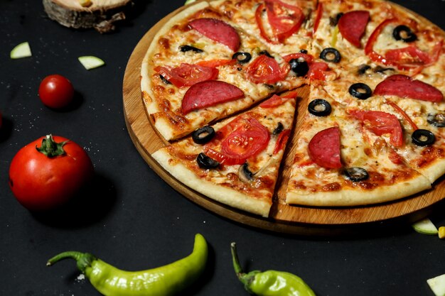 Salami pizza topped with fresh tomato and olive slices close-up view