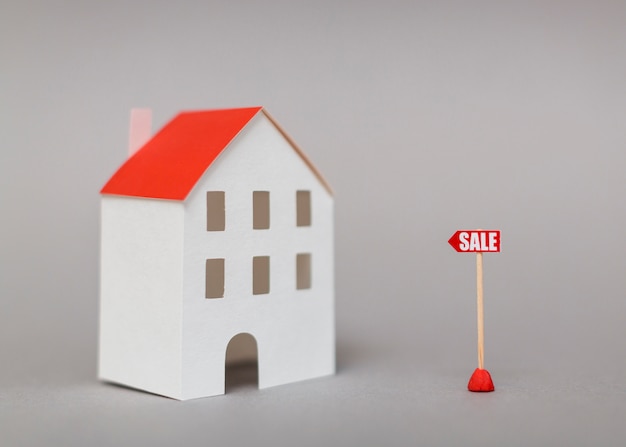 Sale post near the miniature house model against gray background