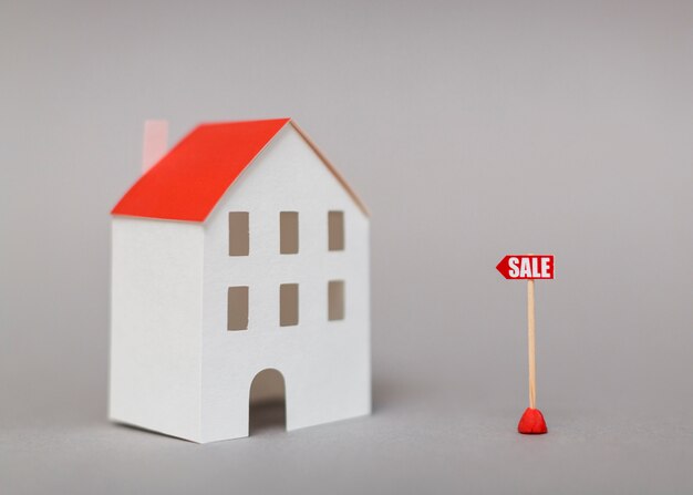 Sale post near the miniature house model against gray background