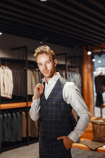 Sale, shopping, fashion, style and people concept. Elegant young man choosing clothes in mall or clothing store.