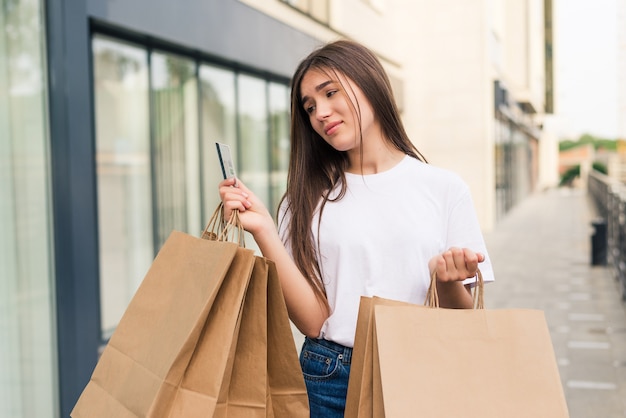 Sale and tourism, happy people concept - beautiful woman holding credit card with shopping bags in the ctiy