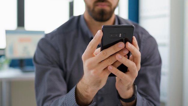 Sales consultant browsing internet on mobile phone in startup office, using smartphone to create financial project. male employee texting messages and working on business growth.