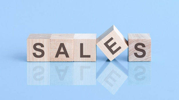 Sales sign made of blocks on a table with a reflective surface, blue background. dice are reflected on the surface with the inscription.