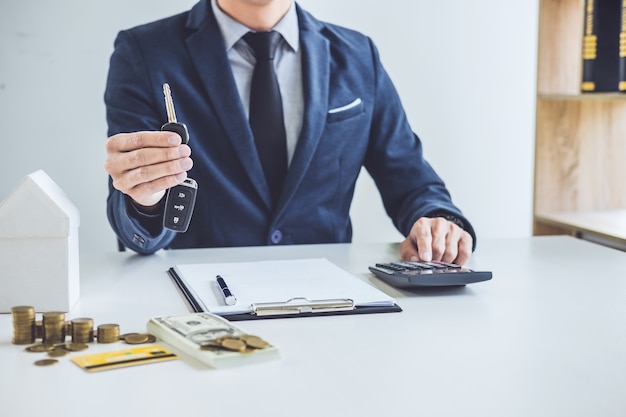 Salesman holding a key and calculating a price of selling new car and home loan