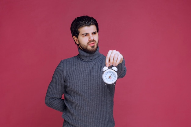 A salesman holding a white alarm clock and promoting it to the customer. 