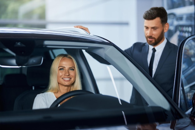 Free photo salesman presenting new luxury car for woman at showroom