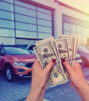 Salesman selling auto in car shop or businessman buying new car holding dollar in hand
