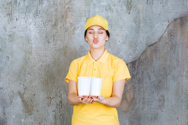 黄色い制服を着たセールスウーマンが2杯のプラスチック製の飲み物を持ってキスを吹いています。